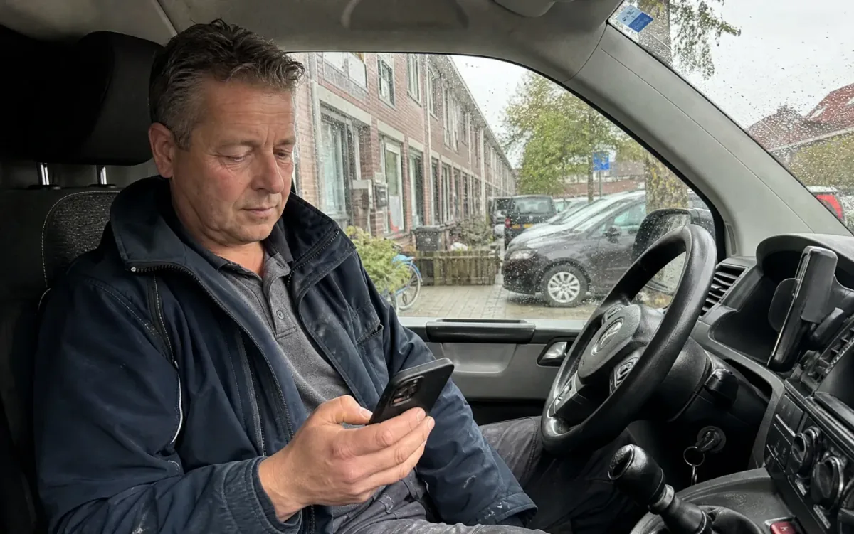 Vakman zit na de werkdag in zijn bus en bekijkt zijn telefoon